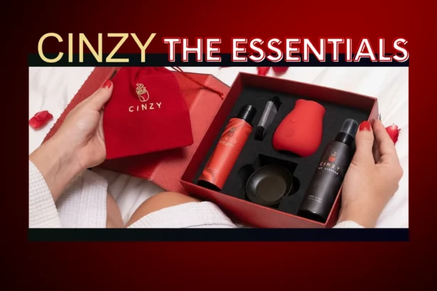 Cinzy The Essentials luxury rose toy gift set. Woman in white bathrobe holding the elegant red gift box containing the Cinzy rose clit vibrator, lube, toy cleaner, and accessories on white bedding with rose petals.